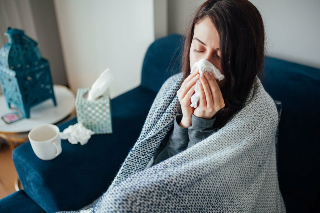 mujer soplándose la nariz durante temporada gripal y cubriéndose con una manta